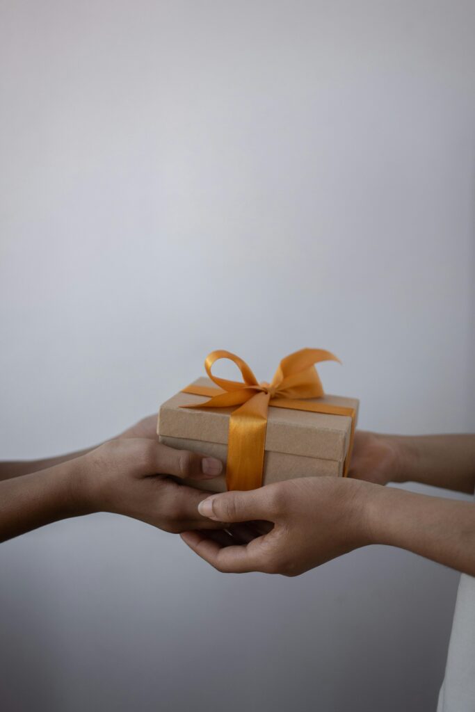 Hands exchanging a wrapped gift box with an orange ribbon, symbolizing generosity.